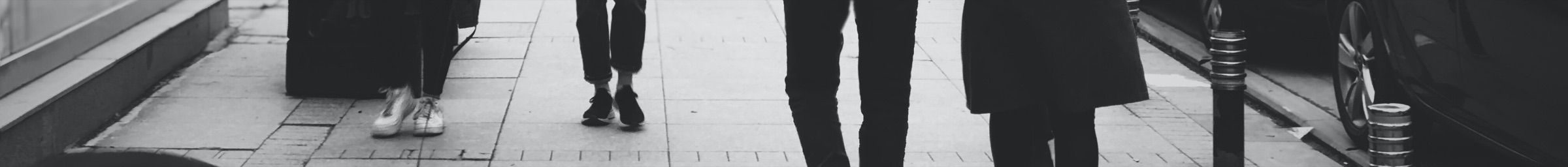 People walking along a city pavement, seen at ankle height in black and white